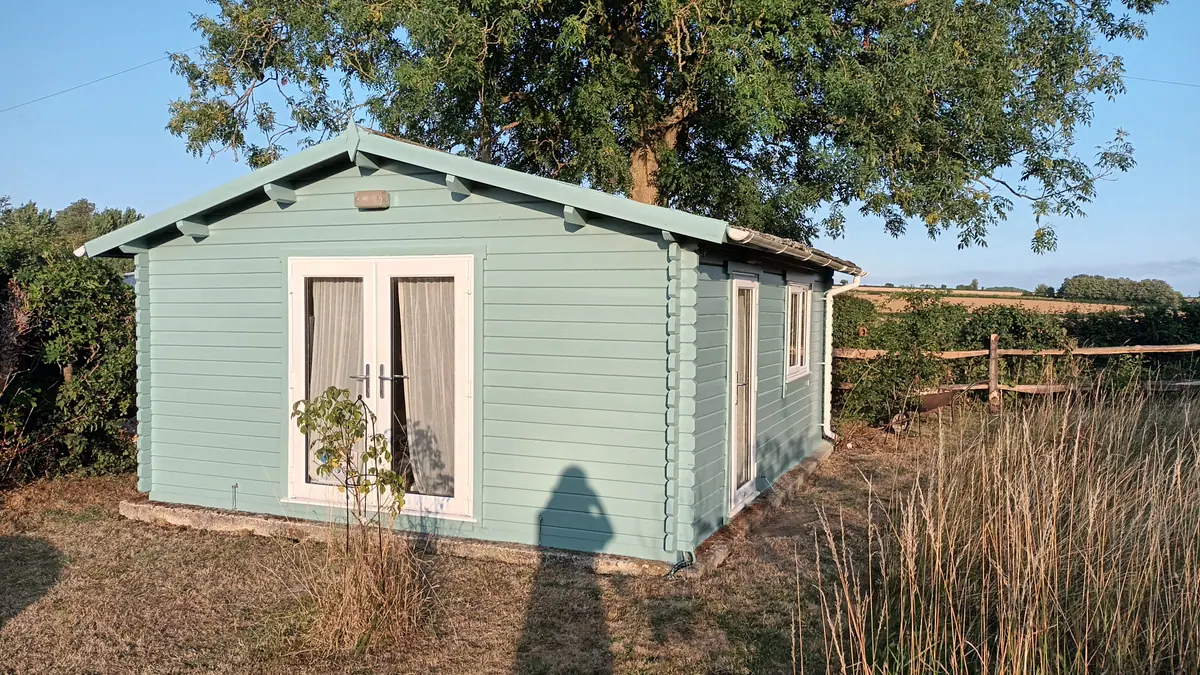 The studio: a pale green timber building at the top of the garden, with fields beyond.